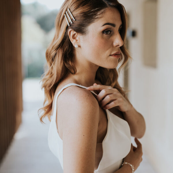 Mariée vue de profil, avec les cheveux détachés, portant des bijoux de mariage en forme de barette perlées dans sa coiffure.