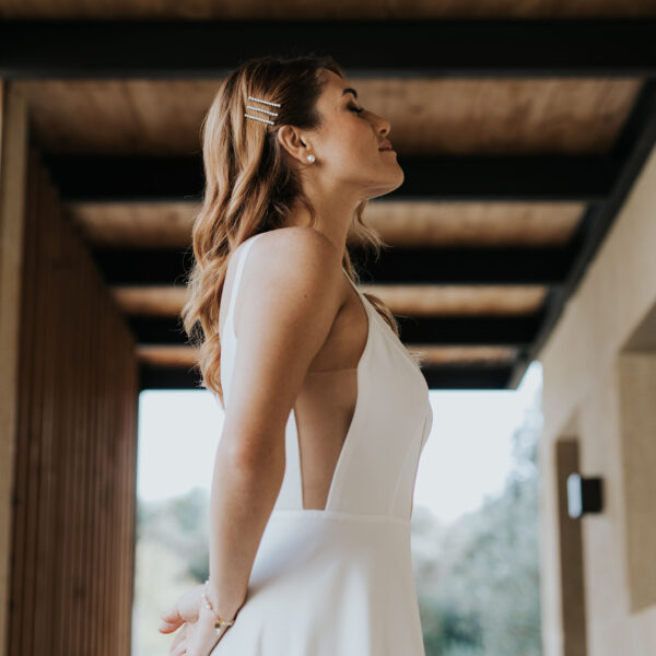 Mariée vue de profil, avec les cheveux détachés, portant des bijoux de mariage en forme de barette perlées dans sa coiffure.