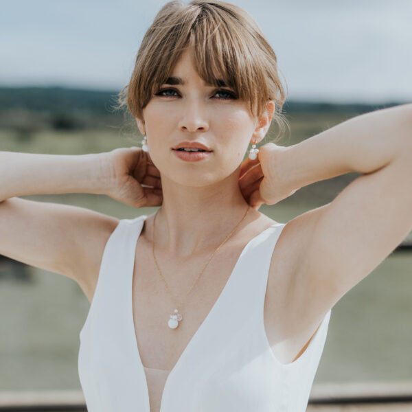 jeune mariée portant ses bijoux de mariage en perles d'eau douce et en porcelaine. Elle porte un collier pendant et des boucles d'oreilles.