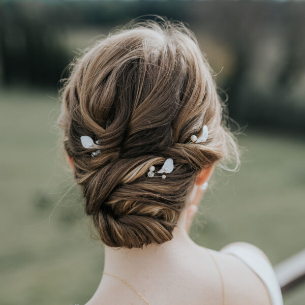 Coiffure de mariée habillée d'épingles à cheveux. Ces bijoux de mariage sont en perles d'eau douce et en porcelaine.