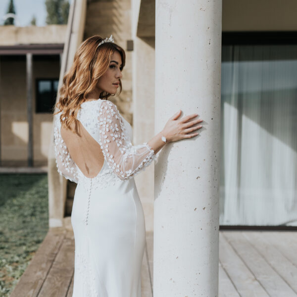 Mariée vue de dos portant ses bijoux de mariage. Elle porte une couronne en feuilles de porcelaine, un bijou de dos en porcelaine et un bracelet coordonné.