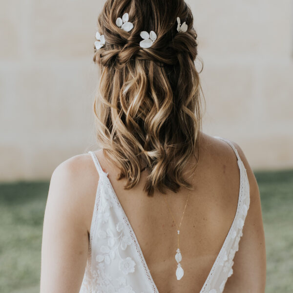 Bijoux de mariage portés par une mariée. Elle porte un collier de dos avec deux pétales en porcelaine montés sur un fine chaîne, et dans ses cheveux d'élégantes epingles à cheveux en porcelaine et perle.