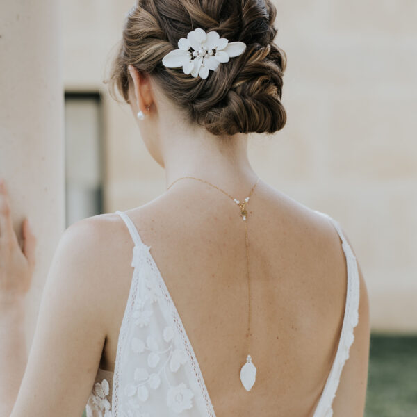 Jeune mariée portant une robe dos nu et des bijoux de mariage en porcelaine. Elle porte un pendentif de dos et dans ses cheveux, un ornement floral en porcelaine.