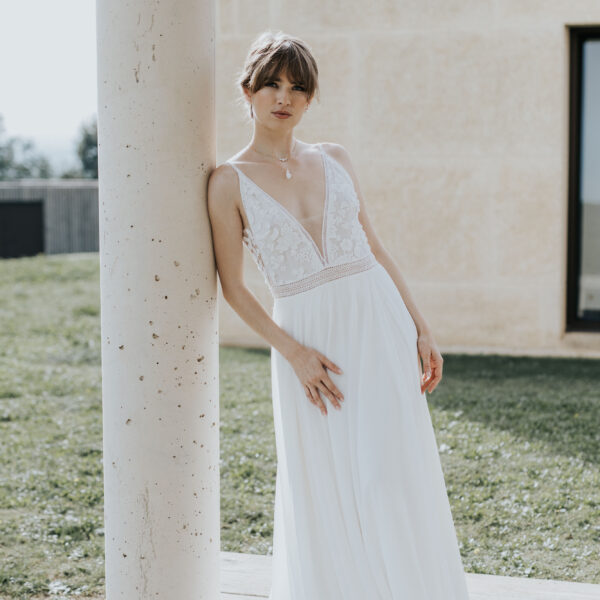 Mariée adossée à un pilier, portant ses bijoux de mariage en porcelaine et perles de Swarovski.