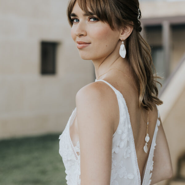 bijoux de mariage en porcelaine portés par une mariée. Elle porte un collier de dos avec des feuilles en porcelaine rehaussées de perles, et des grandes boucles d'oreilles en porcelaine.