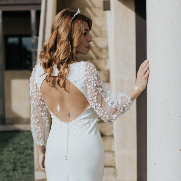 Mariée vue de dos portant ses bijoux de mariage. Elle porte une couronne en feuilles de porcelaine, un bijou de dos en porcelaine et un bracelet coordonné.