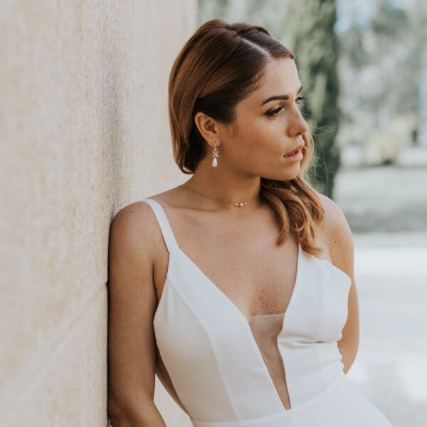 Jeune mariée portant ses bijoux de mariage. La parure se compose d'un collier simple et délicat avec de perles et du cristal de Swarovksi, et des boucles d'oreilles avec gouttes.