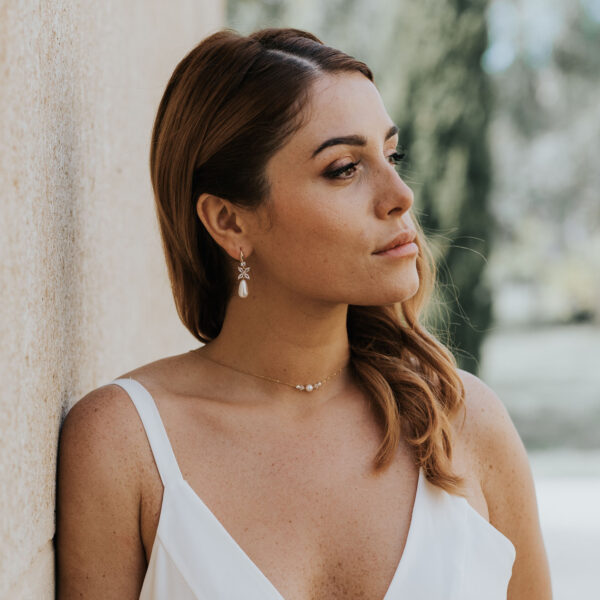 Jeune mariée portant ses bijoux de mariage. La parure se compose d'un collier simple et délicat avec de perles et du cristal de Swarovksi, et des boucles d'oreilles avec gouttes.