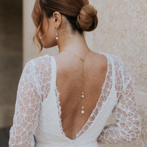 Bijoux de mariage élégants et minimalistes en perle d'eau douce et porcelaine, portés par un mariée. Elle porte des boucles d'oreilles pendantes et sur une robe dos nu, un pendentif de dos.