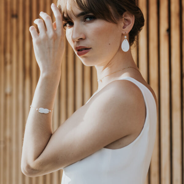 Mariée portant ses bijoux de mariage en porcelaine minimalistes et élégants. Elle porte des boucles d'oreilles et un bracelet.