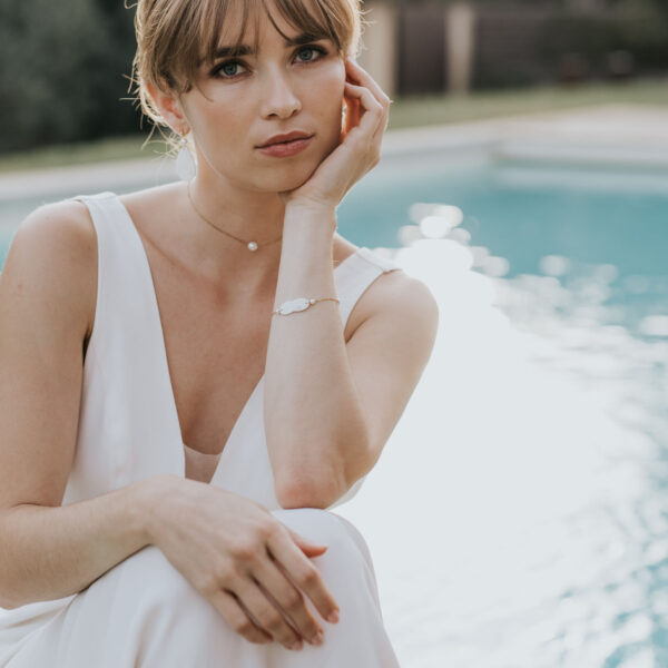 un mariée, au bord d'une piscine, porte ses bijoux de mariage. Elle porte une perle en collier et un bracelet en porcelaine et perles de Swarovski.