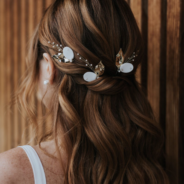 Mariée aux cheveux lachés portant des bijoux de cheveux en porcelaine, perles et feuilles dorées.