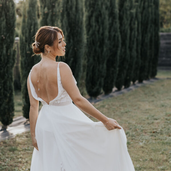 Dans un paysage provençale, une mariée porte ses bijoux de mariage. Sur sa robe dos nu, elle porte un pendentif de dos et dans son chignon de mariée des épingles à cheveux.