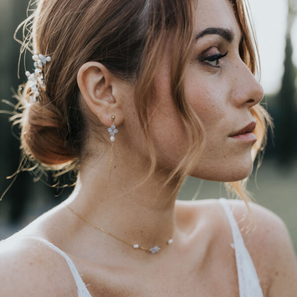 Portrait d'une mariée portant ses bijoux de mariage. Elle porte un bijou de cheveux, un collier fin et des boucles d'oreilles pendantes en perles d'eau douce et perles bleu opal.