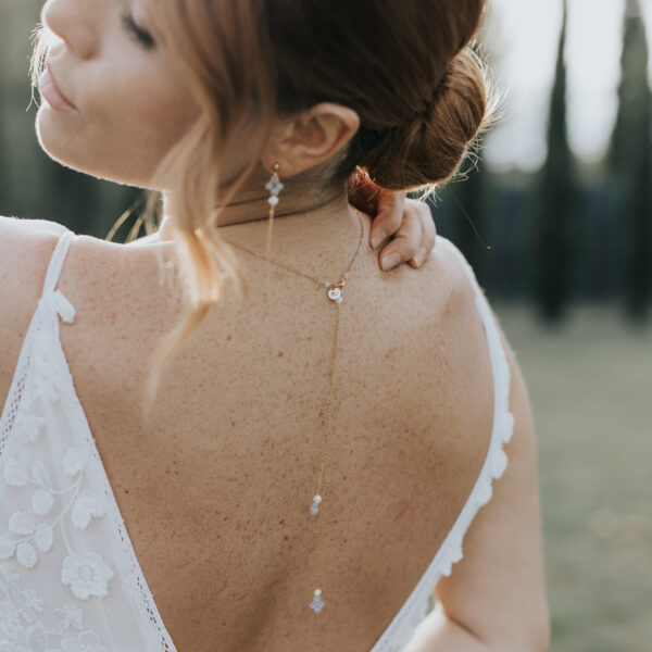 Jeune mariée vue de dos, portant un pendentif de dos et des boucles d'oreilles. Ces bijoux de mariage sont en perles d'eau douce et perles bleu opal.