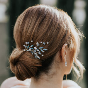 Coiffure de mariée représantant un chignon structuré bas, habillé d'un ensemble de bijoux de cheveux en perle d'eau douce et perle bleu opal.