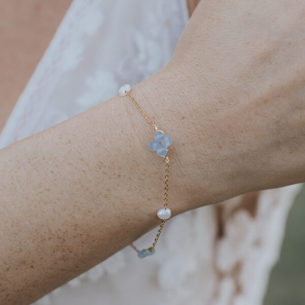 Bracelet en perles d'eau douce et perles bleu opal, monté sur une fine chaîne, au poignet d'une mariée.