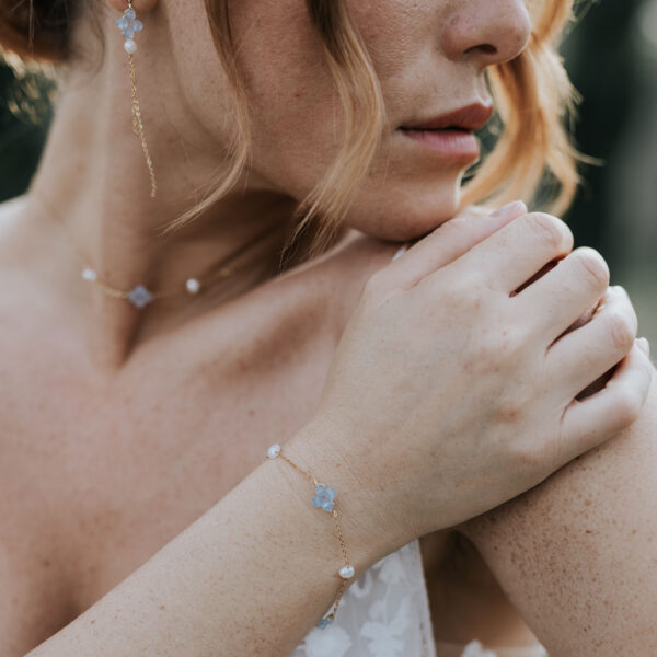 Portrait d'une mariée, la main posée sur l'épaule. Elle porte un bracelet, un collier et des boucles d'oreilles en perles d'eau douce et perles bleu opal, montés sur une fines chaîne.