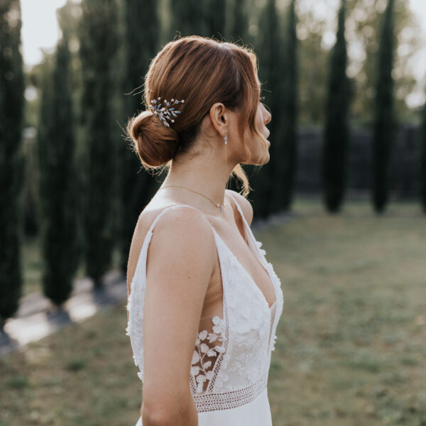 Epingles à cheveux pour coiffure de mariage, portées par une mariée vue de profil. Des boucles d'oreilles fines et pendantes et collier ras de cou en perles d'eau douce et perle bleu opal complète sa tenue.